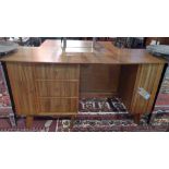 A mid century teak desk, with an shaped top over an arrangement of drawers and cupboard doors on