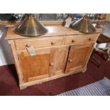 A late Victorian pine dresser base with twin drawers over cupboard doors raised on bracket supports,