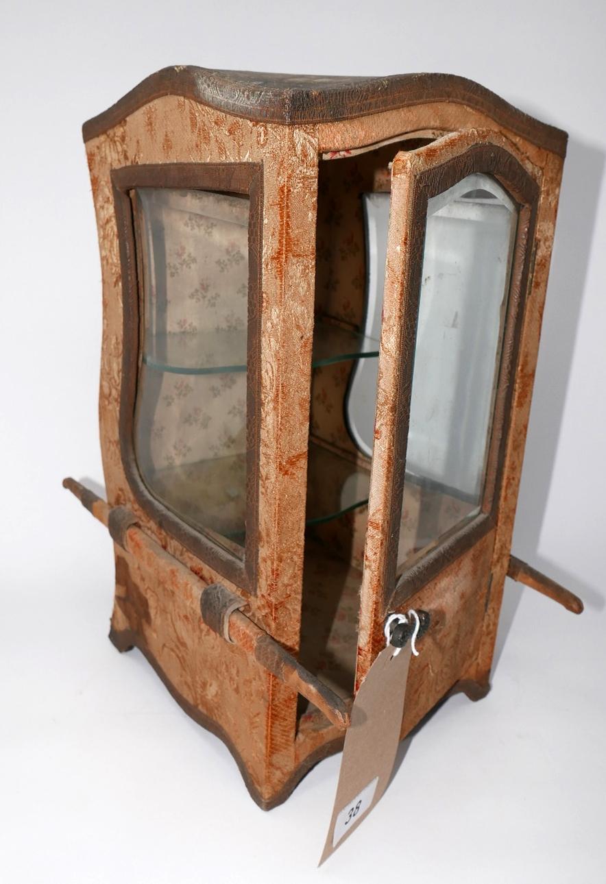 A Victorian carriage form glazed display case with glass shelves, clad and lined in original fabric,