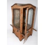 A Victorian carriage form glazed display case with glass shelves, clad and lined in original fabric,