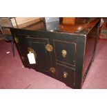 An Oriental black lacquered low cabinet, with twin cupboard doors flanking two small drawers, H.55cm