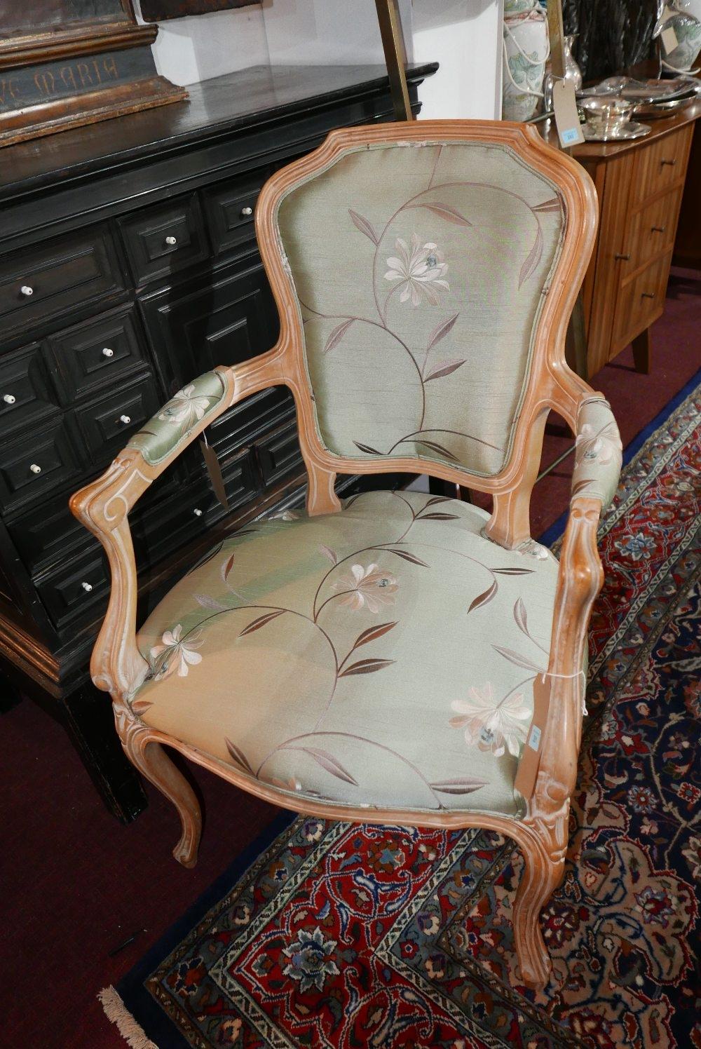A 20th century French limed beech open armchair, with floral silk upholstery raised on carved