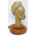 A carved stone bust of an African lady with elaborate coiffure, on stepped circular oak base, H.32cm