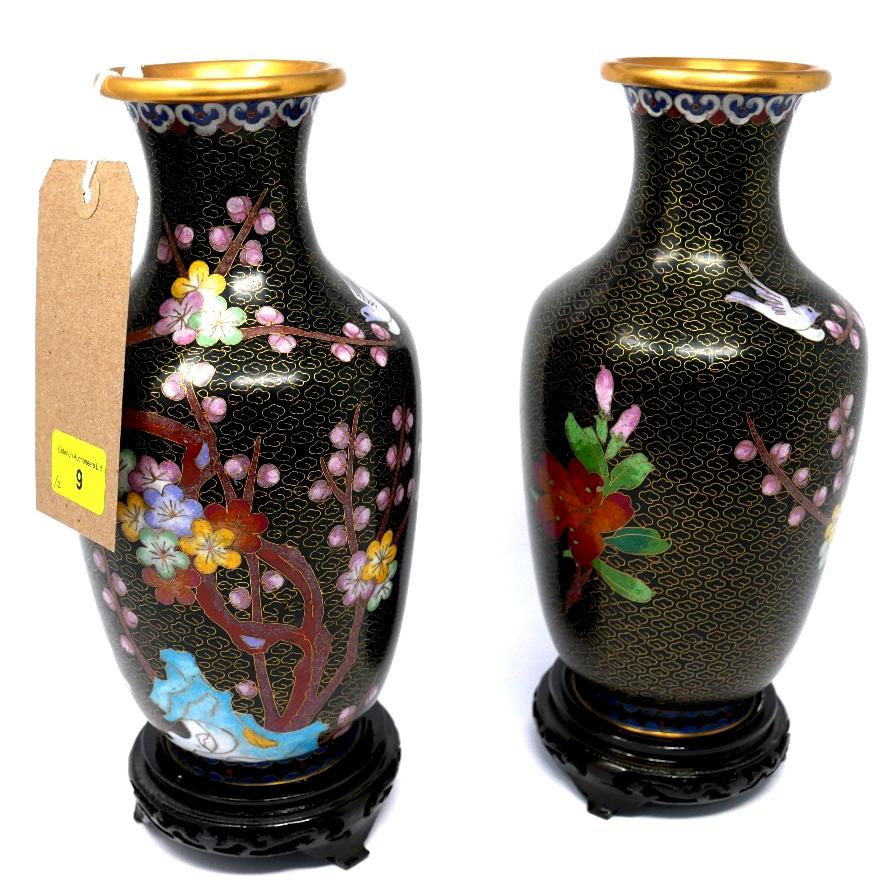 A pair of Chinese cloisonne vases with floral decoration on a black ground, raised on hardwood