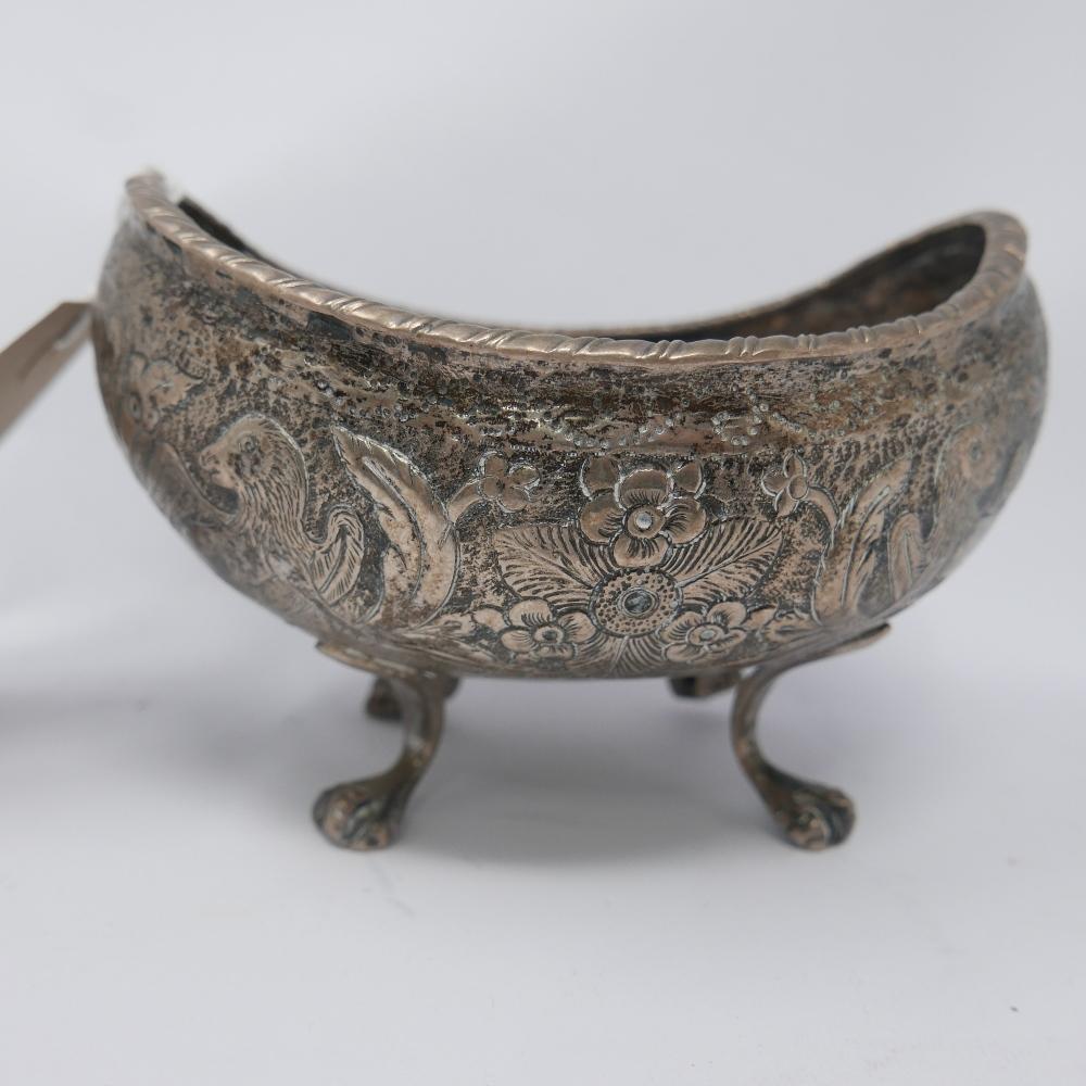 A white metal concave bowl, repousse decorated with griffins amongst flowers, on paw feet