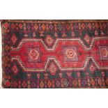 A Persian carpet with triple geometric medallion, on a red and black ground, contained by