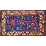A Kazak carpet with triple geometric medallion, on a blue ground, contained by yellow geometric