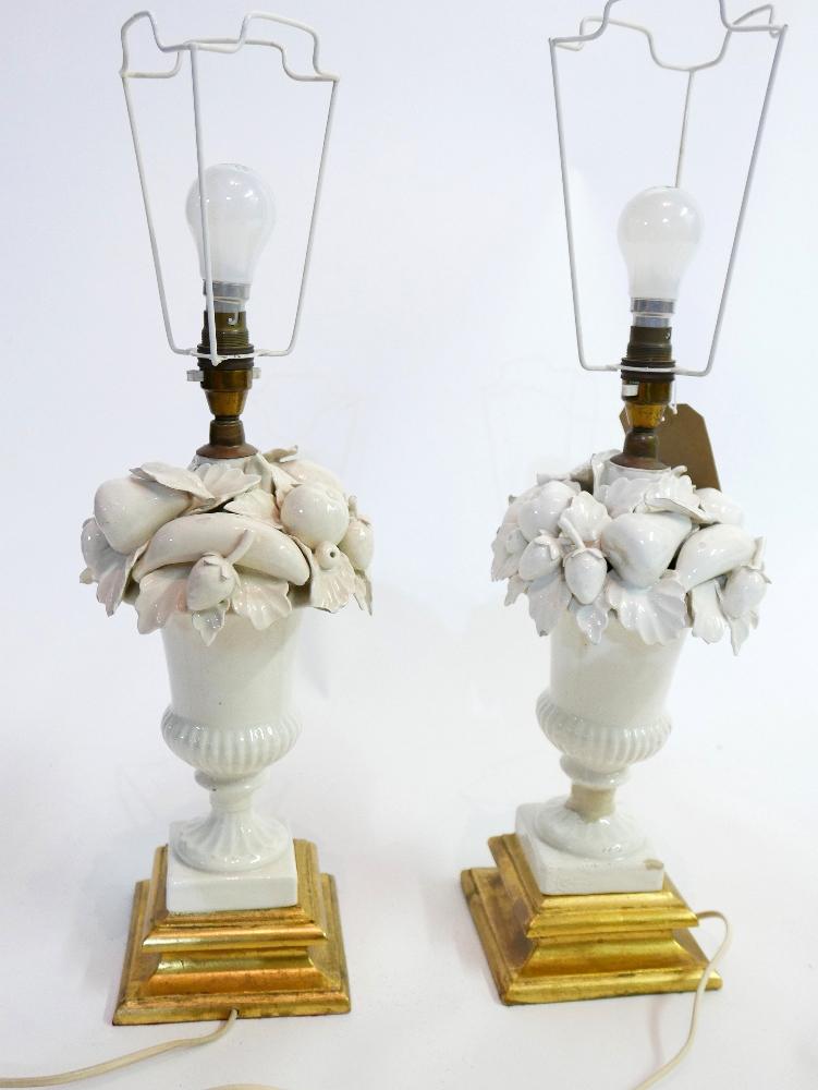 A pair of 20th century white ceramic table lamps in the form of urns of fruit, raised on giltwood