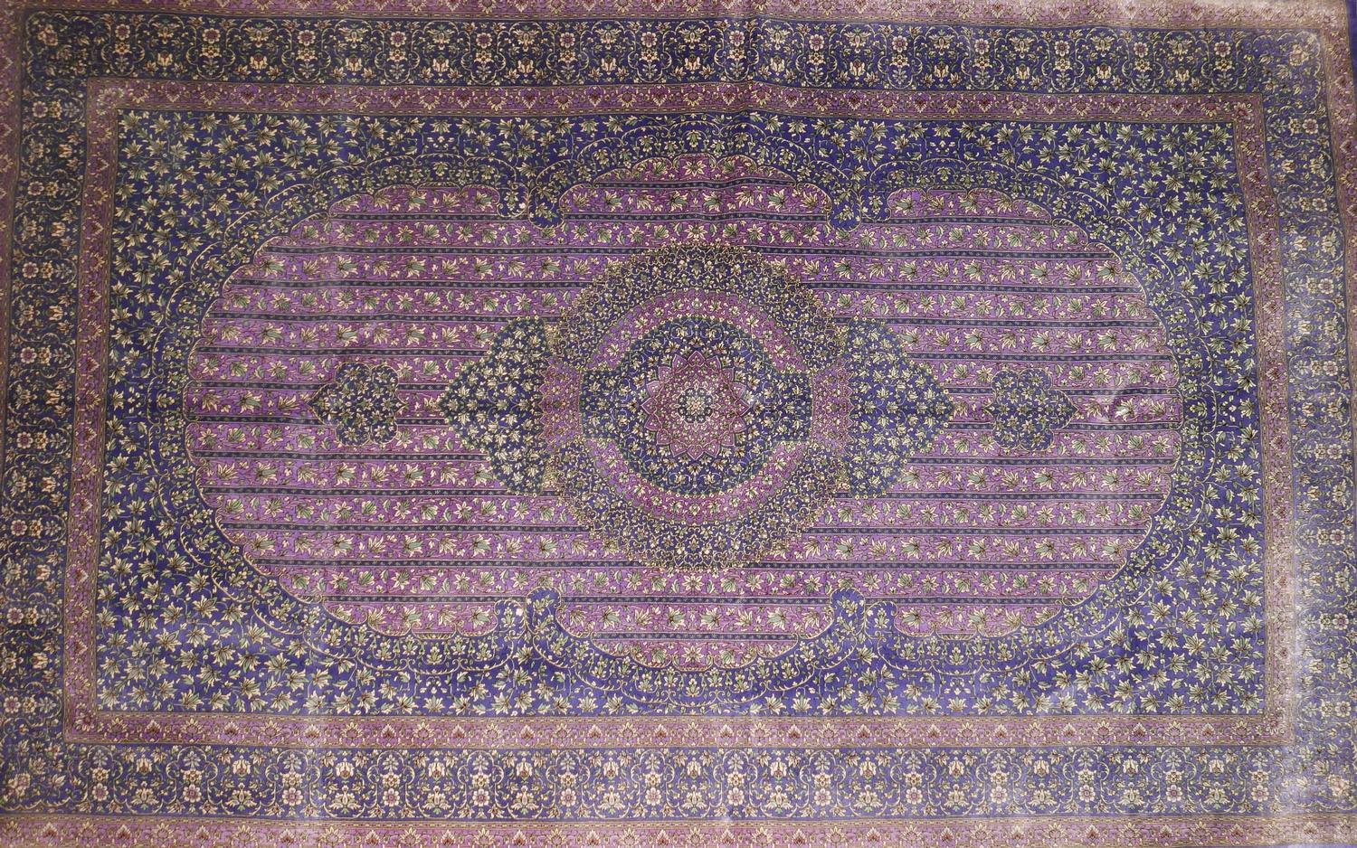 A Qum silk carpet with central floral medallion, on a purple ground, contained by floral motifs