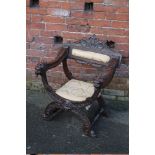 A CARVED OAK ANTIQEU 'X FRAME' ARMCHAIR, heraldic carved detail, the scrolling arms terminating in