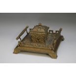 A VICTORIAN BRASS DESK STAND WITH CENTRAL INK WELL, of square form with Gothic styling, the hinged