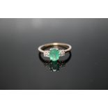 A HALLMARKED 9 CARAT YELLOW GOLD EMERALD RING, set with an oval claw set emerald and eight white