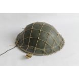 A BRITISH BRODIE TYPE HELMET with camouflage net, dated 1939 to chin strap anchor point