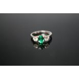 A PLATINUM THREE STONE EMERALD AND DIAMOND RING, set with a central oval emerald measuring approx
