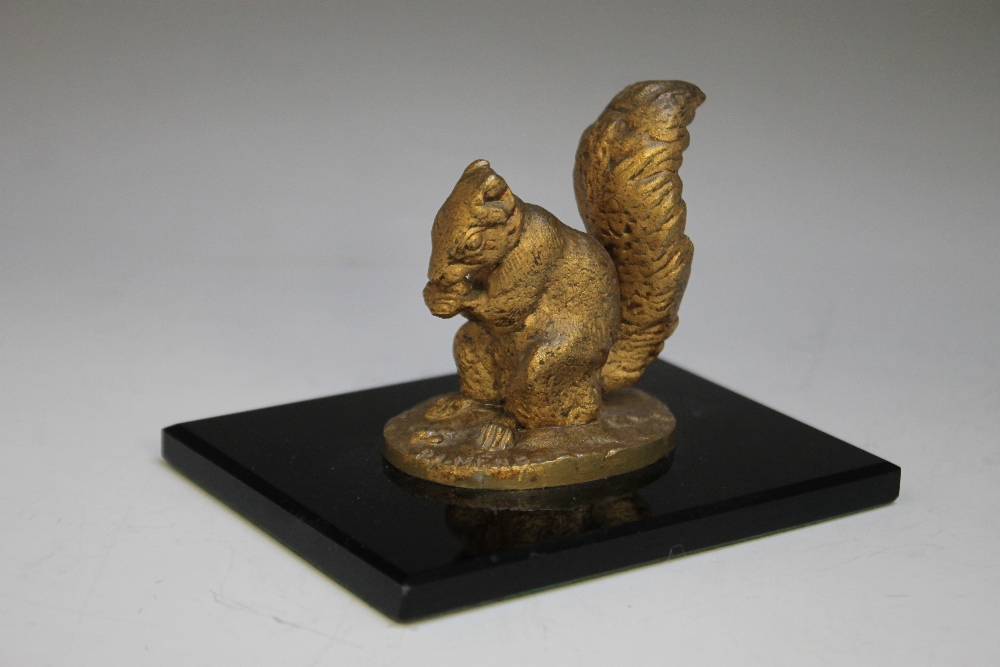 A DECORATIVE DESK WEIGHT IN THE FORM OF A BRONZED GILT SQUIRREL RAISED ON A SLENDER POLISHED ONYX