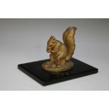 A DECORATIVE DESK WEIGHT IN THE FORM OF A BRONZED GILT SQUIRREL RAISED ON A SLENDER POLISHED ONYX