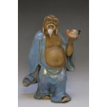 A CHINESE GLAZED FIGURE OF A MAN IN TRADITIONAL ROBES, holding a peach in his outstretched hand,