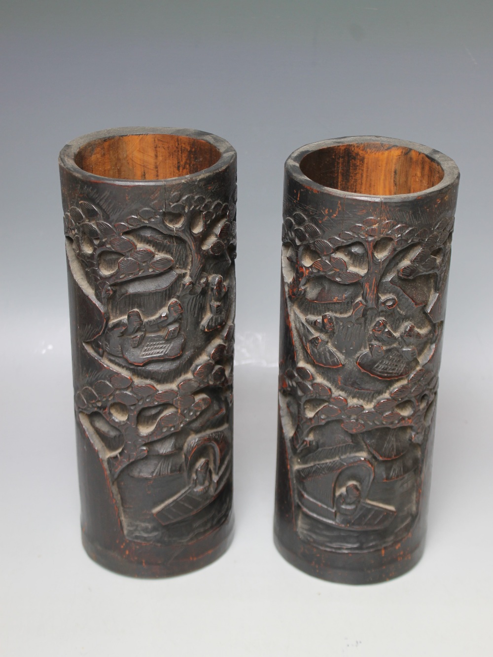 A PAIR OF ORIENTAL HARDWOOD CARVED BRUSH POTS, each typically carved with figures in a wooded