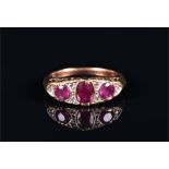 A 9ct yellow gold, ruby, and diamond ring set with three graduated oval cut rubies interspersed with