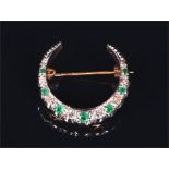 A yellow metal, diamond, and emerald crescent brooch set with alternating round cut stones, 2.9 cm