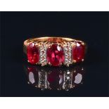A yellow metal, diamond, and synthetic ruby ring set with three oval-cut stones interspersed with