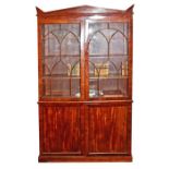 A reproduction mahogany cupboard bookcase in the Victorian style, with an unusual shaped pediment