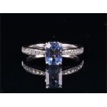 An 18ct white gold, diamond, and sapphire ring set with an emerald-cut pale blue sapphire of