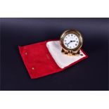 A Cartier travel clock the circular white dial bearing Roman numerals within a gilt metal case, with