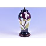 A Moorcroft tubelined pottery table lamp decorated with purple petals, on a graduated blue ground.