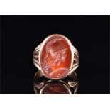 A yellow metal and carnelian ring set with an oval intaglio carnelian engraved with a Classical