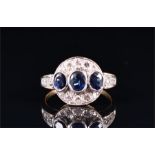 A yellow metal, diamond, and sapphire ring the circular mount collet set with a line of three