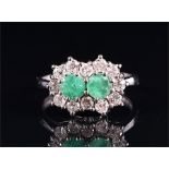 An 18ct white gold, diamond, and emerald cluster ring centred with two round-cut emeralds of