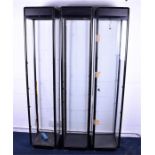 A set of three modern narrow black display cabinets with four glass panels, opening to the back with