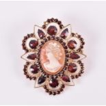 A yellow metal, garnet, and cameo brooch set with an oval cameo of a young lady, within an ornate