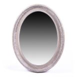 A contemporary decorative oval-shaped wall mirror the distressed Regency style frame with fluted and