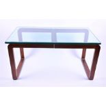 A 1970s-80s teak, metal and glass dining table, with U-shaped teak legs joined by a brass-faced
