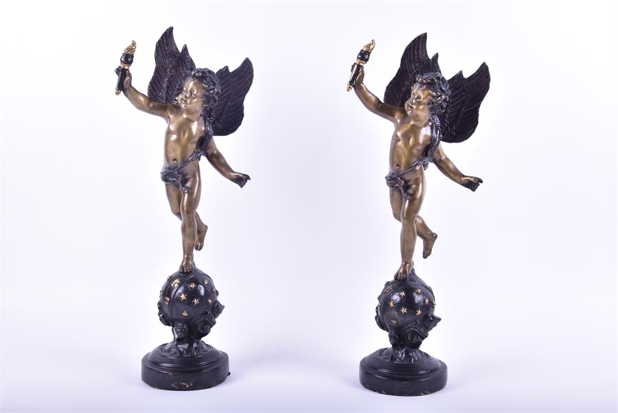 A pair of decorative cast metal figures of winged cherubs each figure standing upon a starred globe,
