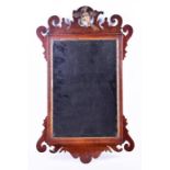 A Georgian mahogany carved mirror designed with scrolls, the top centred with a carved and gilt