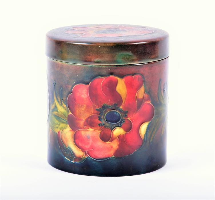 A Moorcroft porcelain lidded cylindrical storage jar the ground in subdued shades of blue and red,