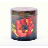 A Moorcroft porcelain lidded cylindrical storage jar the ground in subdued shades of blue and red,