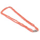 A double strand coral necklace of uneven rounded beads, fastened with a white metal and gemstone
