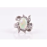 An opal and diamond cluster ring claw-set with an oval cabochon opal, above a stylised ribbon-