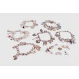 A group of six silver charm bracelets hung with various quantities and types of charms, including