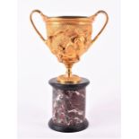A Victorian gilt metal twin-handled trophy or goblet on a polished marble base the bowl decorated