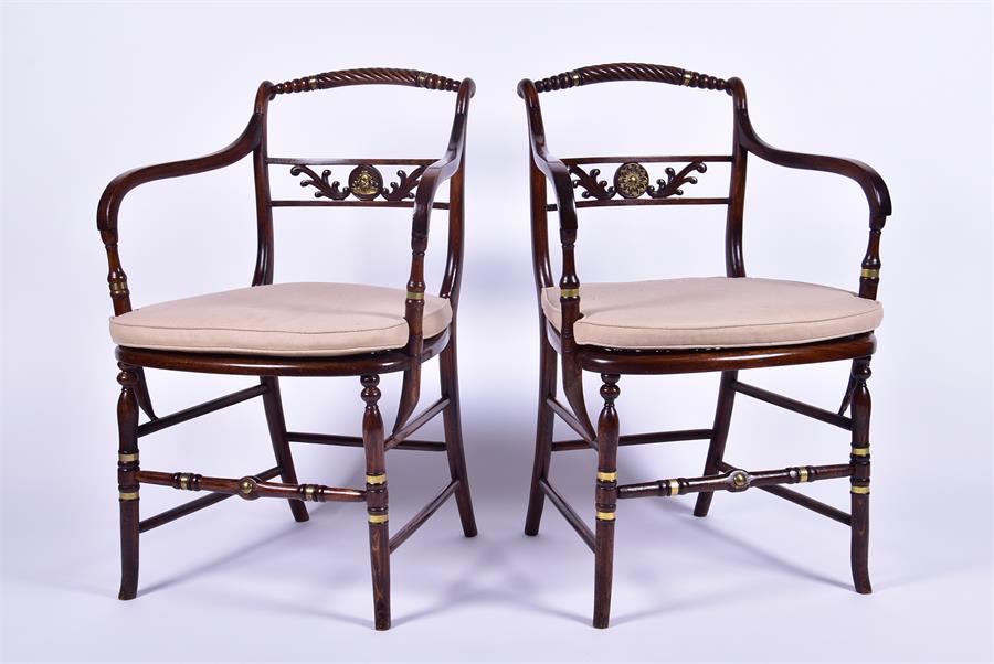 A pair of Regency style stained oak armchairs each with caned seats, applied brass collars and