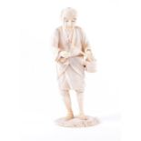 A Meiji period Japanese carved ivory okimono in the form of a walking make figure, carrying a wooden