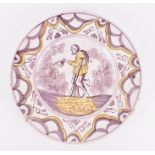 An 18th century English delft pottery charger painted in tones of yellow and purple depicting a