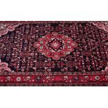 A Hamedan Persian wool carpet with stylised floral motifs within a red border, 300 cm x 160 cm.
