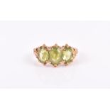 A 9ct yellow gold and peridot ring set with three mixed oval-cut peridot within an ornate gold