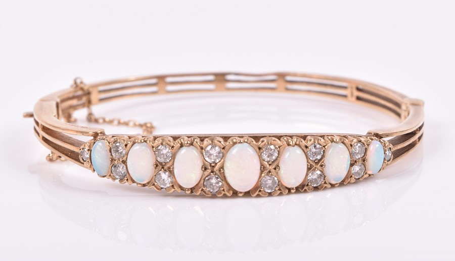 A 9ct yellow gold, diamond, and opal bangle set with seven graduated oval cabochon opals,